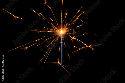 Shiny sparkler with lots of sparks burning bright isolated on black background.