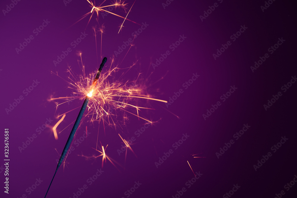 Shiny bright burning bengal fire party sparkler on purple background with copy-space