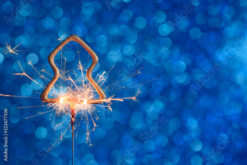Burning golden sparkler in christmas tree shape on blue glitter background with copy-space.