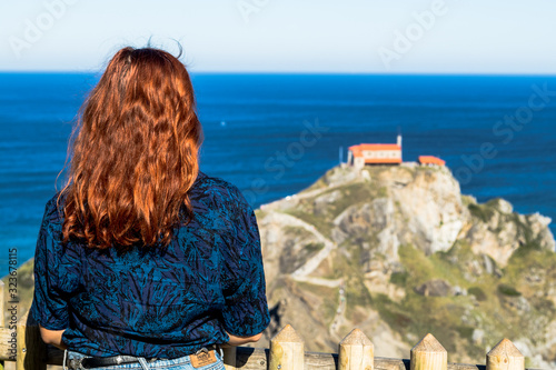 Fototapeta Naklejka Na Ścianę i Meble -  Redhead woman against San Juan de Gaztelugatxe, its medieval stairs and bridge, Basque Country, Spain