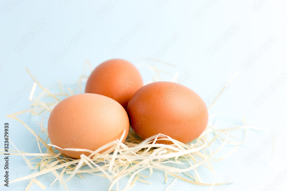 Three Brown Chicken eggs in a Small Nest on the bright blue background. Farm natural products, food or Easter concept. Top view, flat lay Three Brown Chicken eggs in a Small Nest on the bright blue background. Farm natural products, food or Easter concept. Top view, flat lay