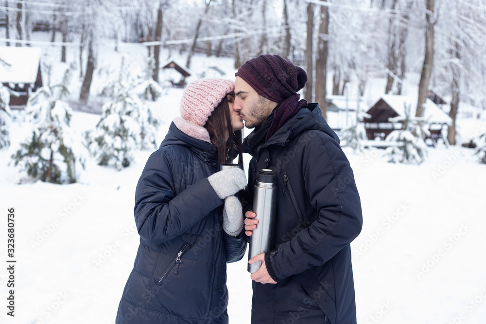 couple kissing while pouring tea from a thermos in winter park couple kissing while pouring tea from a thermos in winter park
