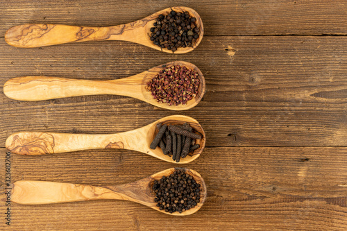 Four wooden cooking spoons made of olive wood filled with different peppercorns on a rustic wooden background whit copy space on the right side