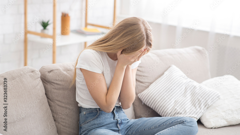 Desperate young woman crying on couch at home Desperate young woman crying on couch at home
