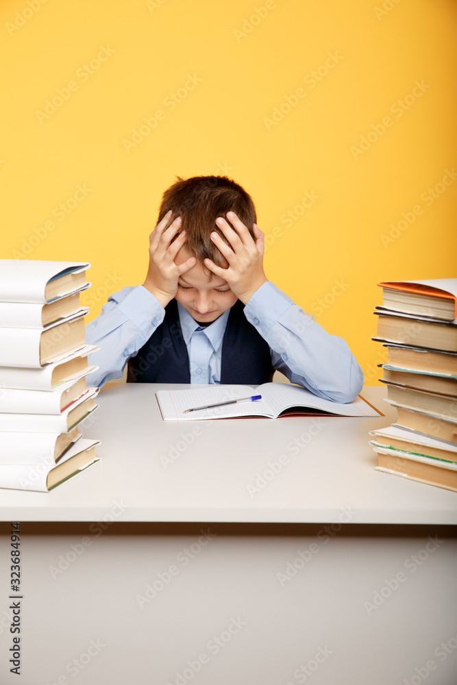 Tired school boy sitting at the desk and studying alone Tired school boy sitting at the desk and studying alone