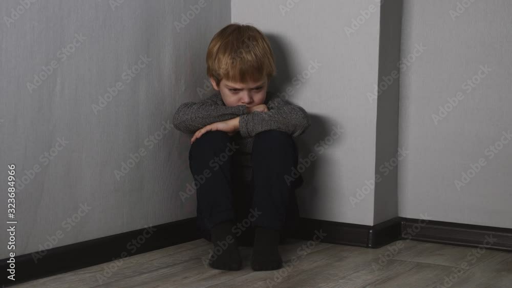 A scared, lonely blond boy sits on the floor in the corner of the room. A scared, lonely blond boy sits on the floor in the corner of the room.
