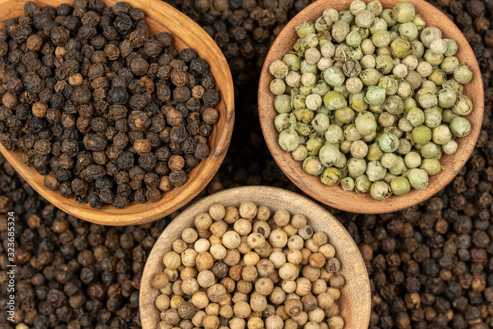 Spice background, Background made of many whole black peppercorns and a cooking spoon made of olive wood and two wooden bowls filled with black, green and white peppercorns , extreme close up Spice background, Background made of many whole black peppercorns and a cooking spoon made of olive wood and two wooden bowls filled with black, green and white peppercorns , extreme close up