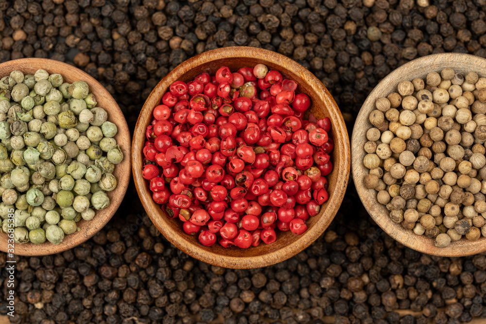 Spice background, Background made of many whole black peppercorns and three wooden bowls also filled with white, green and red peppercorns , extreme close up, top view Spice background, Background made of many whole black peppercorns and three wooden bowls also filled with white, green and red peppercorns , extreme close up, top view