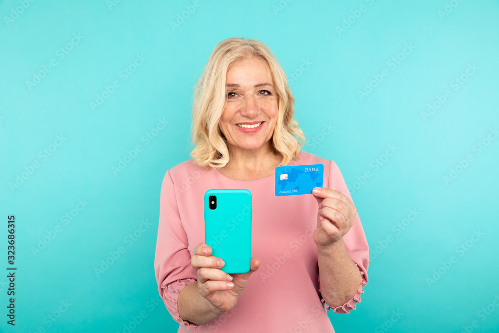 Fototapeta premium Happy woman in the pink dress holding credit card with mobile