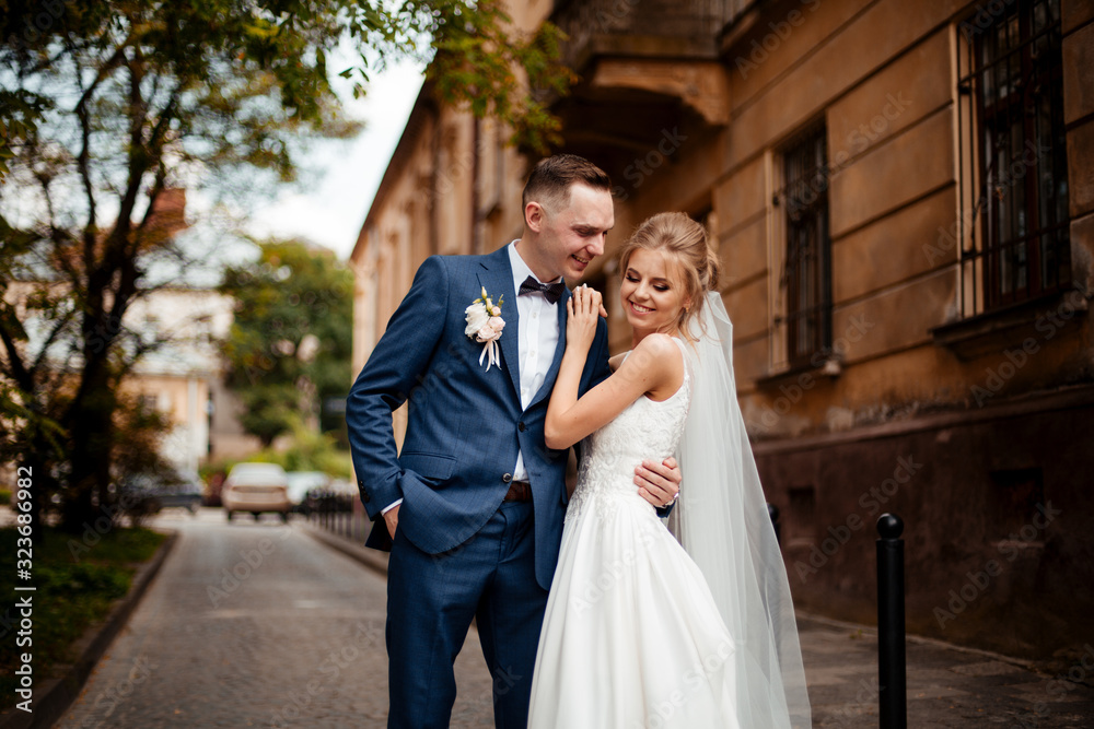 Gorgeous wedding couple walking in the city. Groom in a stylish suit and bride in a beautiful white dress, the couple is walking the streets of the city on their wedding day. Together. Wedding concept