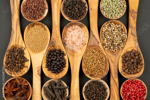 Spice and Food - Background made of many various spices and pepper varieties in small wooden bowls and cooking spoons made of olive wood on a black background