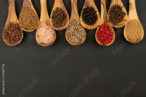 Spice and Food - Nine cooking spoons made of olive wood in a row filled with spice and pepper varieties on a black background with copy space