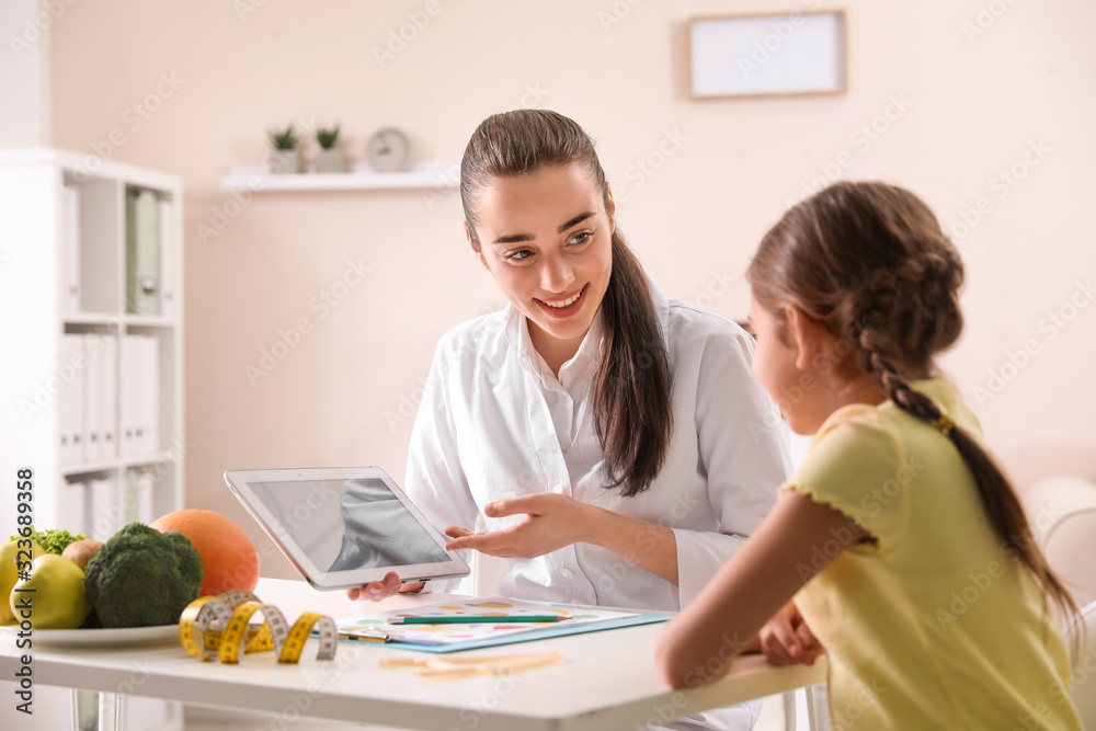 Professional nutritionist with tablet consulting little girl in office Professional nutritionist with tablet consulting little girl in office