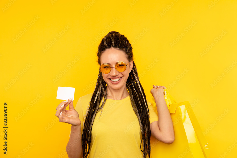 Happy young woman on the yellow background posing with bags and bright phone