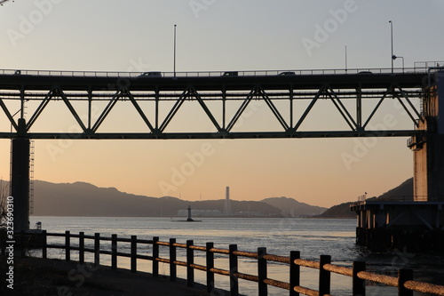 夕景の海と橋と、橋を渡る車 © K.TARAKU