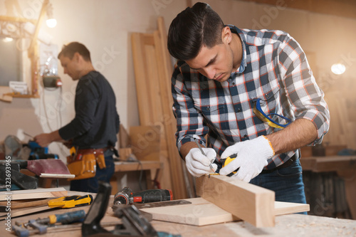 Professional carpenter and colleague working with wooden plank in workshop