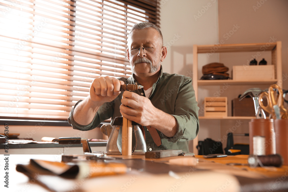 Man burnishing edges of leather belt in workshop