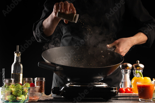 The chef sprinkles seasoning, freezes in motion, prepares a meat dish. Against the background of vegetables. Culinary, Restaurant business, recipes. Restaurant and hotel business
