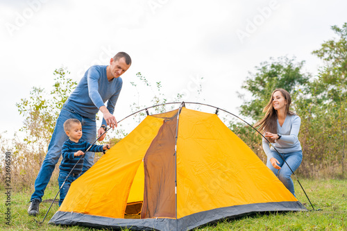 Happy family with little son set up camping tent. Happy childhood  camping trip with parents. A child helps to set up a tent