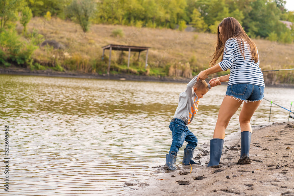 Φωτογραφία Mom with a small son walks along the sandy shore of the lake in rubber boots