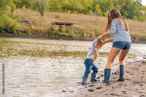 Foto Mom with a small son walks along the sandy shore of the lake in rubber boots