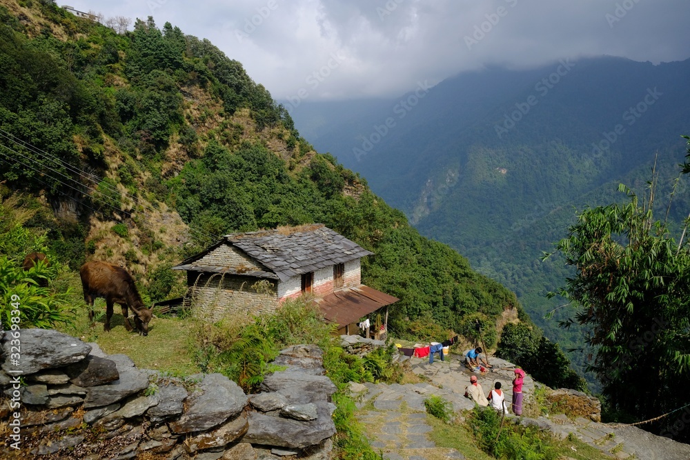 Mountain view with people sitting next to house and terraced fields in Himalaya village, during trekking around Annapurna. 