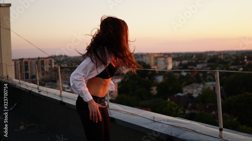 Fototapeta Naklejka Na Ścianę i Meble -  Young girl in sports uniform sits on the edge of the roof during sunset.