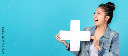 Fotografi Banner of Happy asian woman smiling and holding plus or add sign on copy space blue background