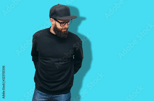 Portrait of handsome hipster guy with beard wearing black blank hoody or sweatshirt and black cap with space for your logo or design. Mockup for print