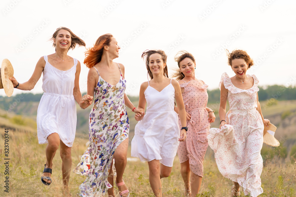 The company of cheerful female friends have a great time together on a picnic in a picturesque place overlooking the green hills. Girls in white dresses dancing in the field The company of cheerful female friends have a great time together on a picnic in a picturesque place overlooking the green hills. Girls in white dresses dancing in the field