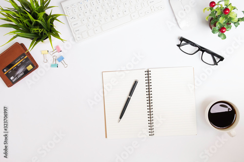White office desk table with white keyboard, notebook, pen, eyeglasses, document clips, brown wallet and credit card, cup of black coffee , top view, flat lay with copy space