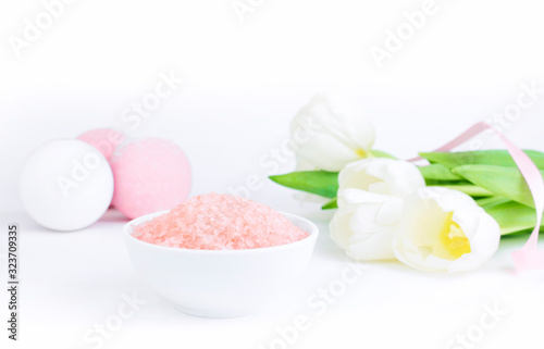Pink bath salt next to salt bombs and tulips, on a white gray background, are reflected on the mirror surface of the table. The concept of cosmetology, spa care, relaxation. Copy space