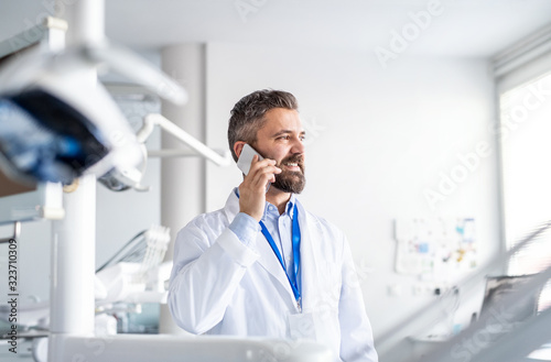 Mature dentist in modern dental surgery, using smartphone.