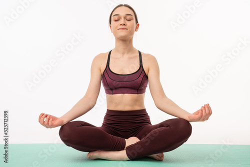 Attractive young female with brown hair practicing yoga posture on mat against wall in studio