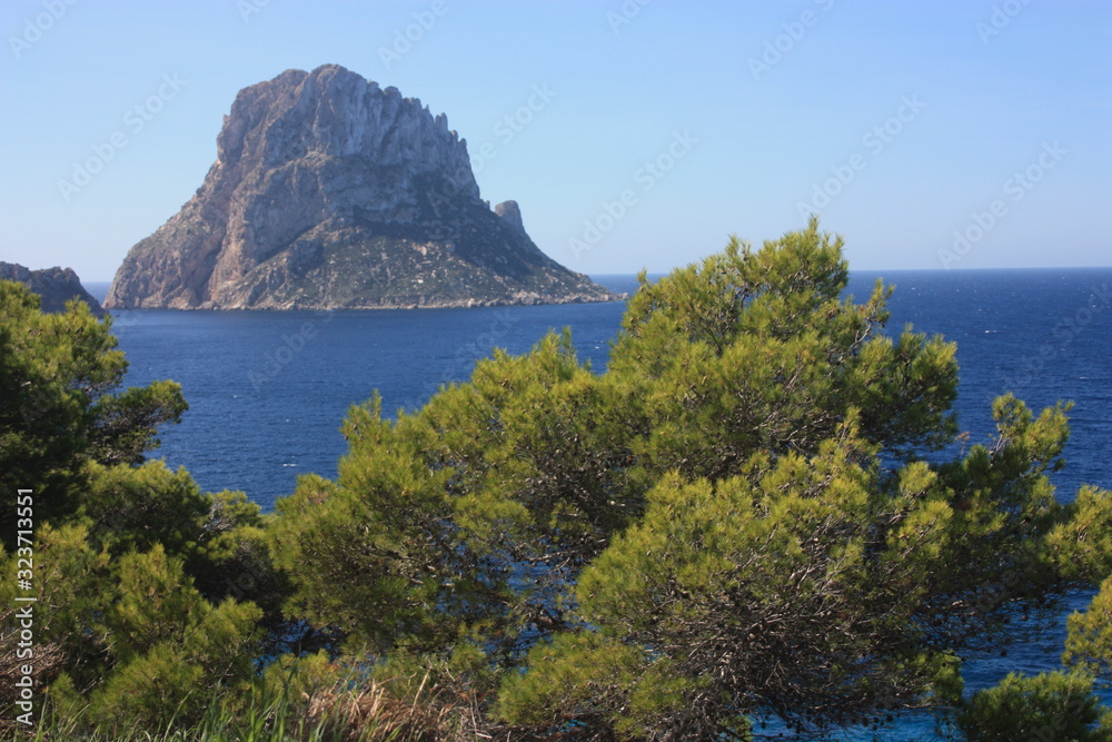 The island of Es Vedra between the blue sky and the blue sea of the Ibizan coasts in front of the Cala D'Hort beach in the Balearic Islands The island of Es Vedra between the blue sky and the blue sea of the Ibizan coasts in front of the Cala D'Hort beach in the Balearic Islands