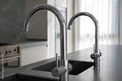 Modern square kitchen sinks and polished chrome faucets installed on a dark grey granite kitchen island, luxurious and minimalist design for homes using durable materials and contemporary appliances