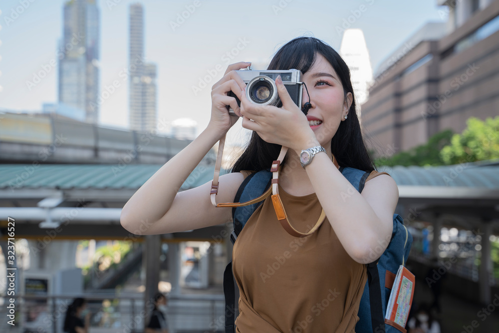 Outdoor summer smiling lifestyle portrait of pretty asian young woman having fun in the city thailand with camera travel photo.