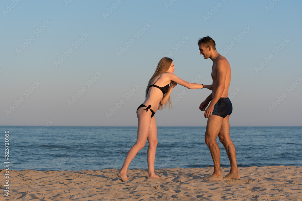 The girl beats a man in the stomach with his fist on the sandy seashore