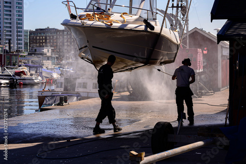 2 people pressure washing hanging boat in marina