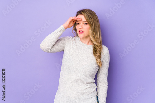 Young caucasian woman isolated on purple background looking far away keeping hand on forehead.