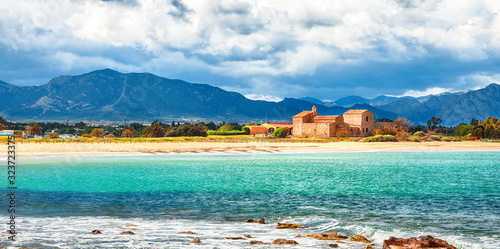 The Nora bay and beach, the medieval Sant'Efisio church near the shore and mountains in the background photo
