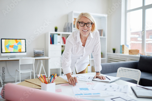 Portrait of smiling mature woman looking at camera while working with designs in modern office, copy space photo