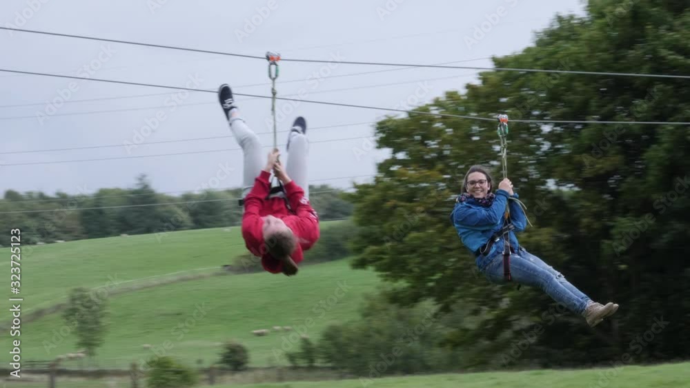 Two Girls hanging on Zip Wire / line - Aerial runway adventure in the outdoors. Slow Motion. 4K stock Video Clip Footage