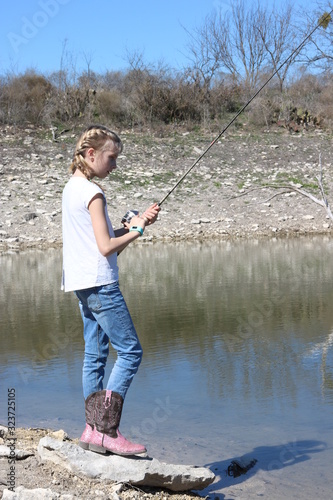 Blonde young girl with french braids and cowboy boots fishing in the lake