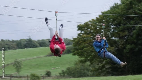 Two Girls hanging on Zip Wire / line - Aerial runway adventure in the outdoors. Slow Motion. 4K stock Video Clip Footage photo