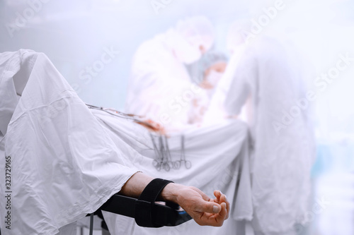 Hand of patient on operating table, doctors are operation person. Light blue background