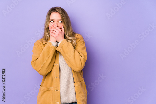 Young caucasian woman isolated on purple background thoughtful looking to a copy space covering mouth with hand.