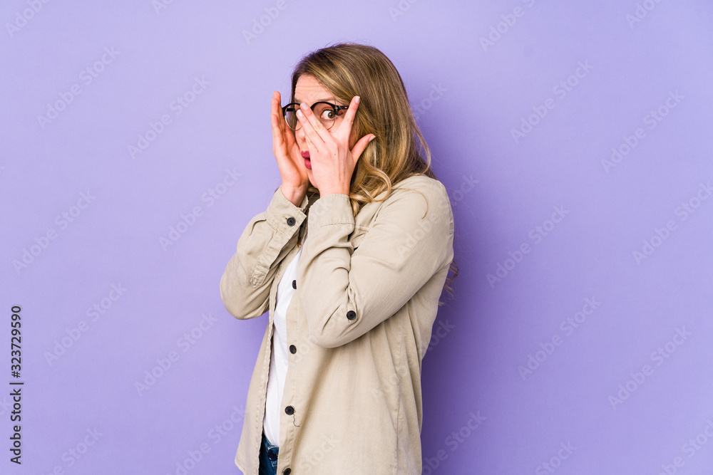 Young caucasian woman isolated on purple background blink through fingers frightened and nervous. Young caucasian woman isolated on purple background blink through fingers frightened and nervous.