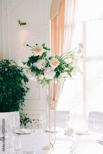 beautiful floral arrangement of delicate rose flowers and fresh greenery in the design of the wedding table in the white hall