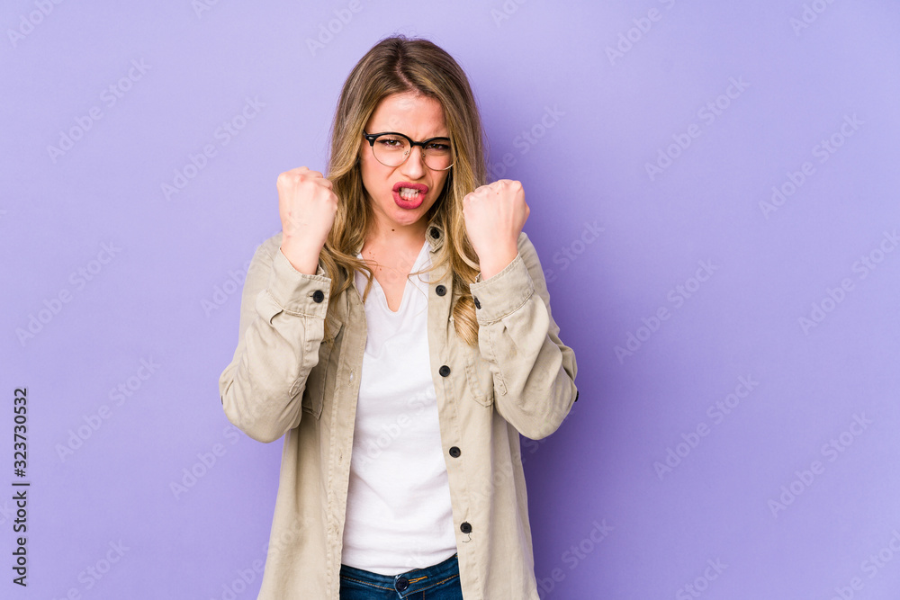 Young caucasian woman isolated on purple background showing fist to camera, aggressive facial expression.